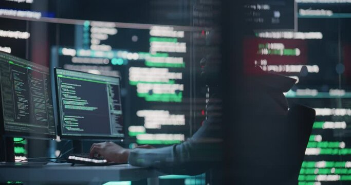 Dolly Shot of a Black Male Programmer Working in a Monitoring Control Room, Surrounded by Big Screens Displaying Lines of Programming Language Code. Portrait of a Man Creating a Software and Coding