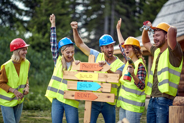 A group of cheerful both female and male builders posing for a photo at a cottage construction...