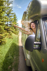 beautiful blonde enjoying the wind driving in the nature with her head out of the vehicle window, laughing