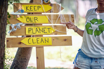 Young activist showing to wooden board saying, Keep our planet clean. Volunteers in nature picking...