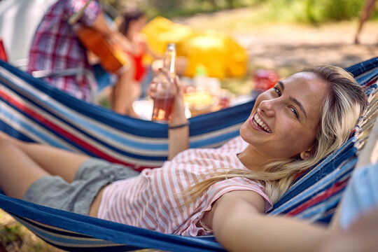 Young cheerful hipster woman taking selfie while laying in hammock and holding beer. Young man and woman enjoying holiday. Holiday, togetherness, fun, lifestyle concept.