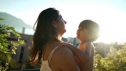 Small boy kissing mother in cheek outside during sunset. Mother holding affectionate child during...