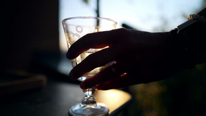 Serving white wine on glass outside in sunset time. Hand picking cup with alcoholic beverage