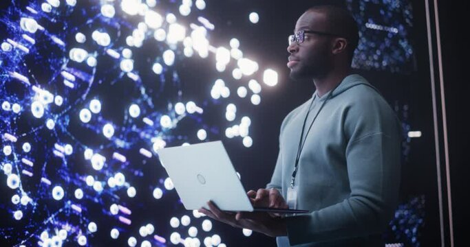 Portrait of Young Black Man Working on Laptop Computer, Looking at Big Digital Screen Displaying Neural Network Visualisation 3D Animation. Professional Data Specialist Analysing User Information