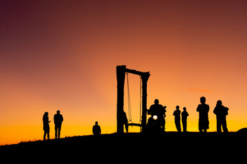 Group of people on top of a mountain in sunset. Silhouette of friends on hill and swing with golden sunset background. hikers celebrating success on top of a hill in the sunset