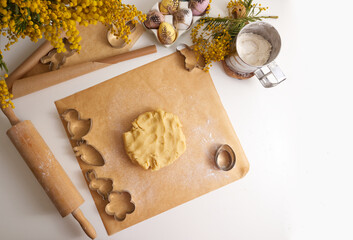 Fresh dough on baking paper close-up against the background of a vase with a bouquet of mimosa