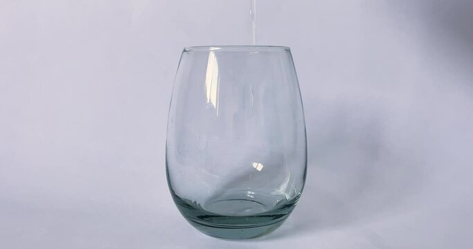 Water being poured in an oval glass cup, in slow motion.