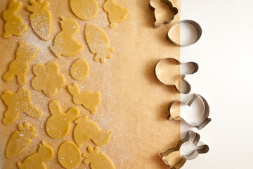 Raw Easter cookies and cookie cutters on baking paper top view