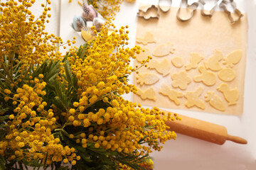 Yellow mimosa close-up against the background of the preparation of Easter cookies from fresh dough