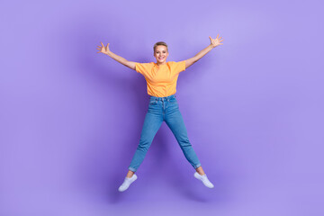 Fototapeta na wymiar Full length photo of pleasant adorable girl wear jeans white sneakers jumping high like star hands up isolated on violet color background