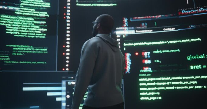 Zoom Out Back View of Young Black Man Looking at Big Digital Screens Glitching While Displaying Code Lines. Professional Hacker Breaking Through Cybersecurity Protection System, Changing Code