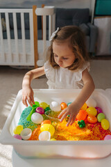 A little girl playing with colored rice and Easter eggs in sensory bin. Easter sensory bin with bright rice and eggs, bunny, carrot. Sensory play and holidays activity for kids. Happy Easter concept.