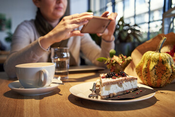 Sweet cake in a coffee bar with a woman photographing with her smartphone
