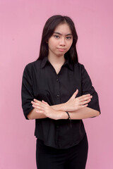 An upset young asian lady in a black polo shirt and arm crossed. Isolated on a light pink...