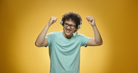 Close up shot of happy asian guy with curly hair putting on headphones and dancing, isolated on...