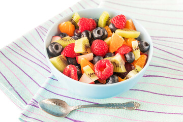 In a ceramic blue bowl, a fruit fresh delicious salad with raspberries, blueberries, kiwi, tangerines, apples.