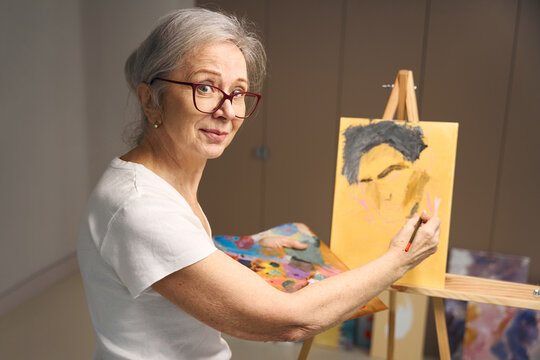 Talented elderly woman stands at an easel with a palette