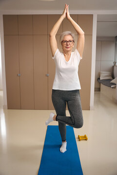 Disciplined retired woman in sportswear is doing yoga at home