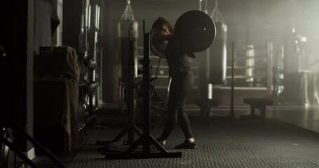 Strong young female athlete squatting with barbell in gym