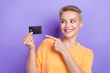 Portrait of charming cheerful girl toothy smile look direct finger arm hold debit card isolated on purple color background