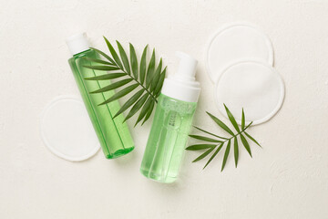 Foaming facial cleanser and micellar water with eco pads on concrete background, top view
