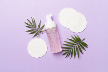 Foaming facial cleanser and with eco pads on color background, top view