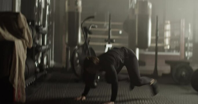 Determined sportswoman doing burpee with push ups exercise in gym