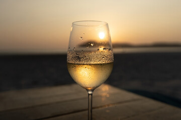 White wine in the misted glass against the sunset sky on the beach