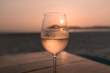 White wine in the misted glass against the sunset sky on the beach