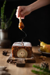 Gingerbread loaf cake with poached pears decorated with honey and icing sugar on a wooden cutting board. Christmas pear loaf cake