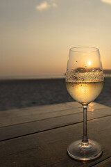 White wine in the misted glass against the sunset sky on the beach