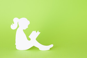 Paper silhouette of a girl reading a book isolated on green background