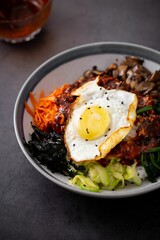 Vertical closeup of a korean meal with vegetables and fried egges in a white bowl