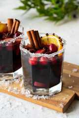 Christmas homemade spicy mulled red wine with cranberries, orange and cinnamon stick on a light background with artificial snow. Traditional hot drink for Christmas.