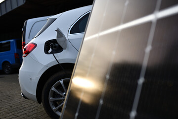 Elektroauto das umweltfreundlich vor einem Solarpanel aufgeladen wird. Sonne spiegelt sich im...
