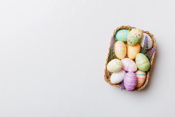Colorful Easter eggs in wicker basket against colored background, closeup. top view with copy space