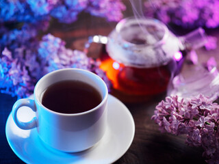 cup of lilac tea on a wooden table. flowering branches of purple lilac, glass teapot