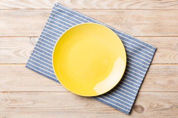 Top view on colored background empty round yellow plate on tablecloth for food. Empty dish on napkin with space for your design