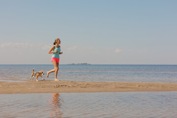 athletic woman and beagle dog run along sandy beach on seashore in morning. healthy lifestyle, train with your pet. fitness and yoga outdoor in nature. do sports for health