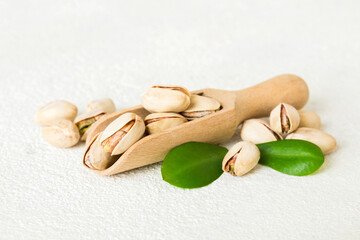 Close-up of tasty pistachio nuts in spoon with leaves on table background. Top view. Flat lay