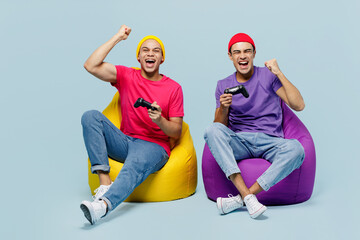 Full body fun young couple two friend men wear casual clothes together sit in bag chair hold play...