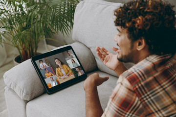 Young Indian man wears casual clothes use digital tablet pc computer leading video conference call lay down on grey sofa stay at home hotel flat rest relax spend free spare time in living room indoor.