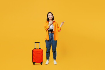 Young woman in summer casual clothes stand near suitcase point finger aside isolated on plain...