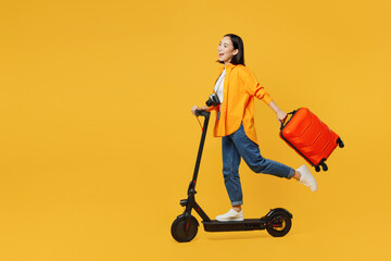 Young woman wear summer casual clothes hold suitcase ride electric scooter isolated on plain yellow background. Tourist travel abroad in free spare time rest getaway. Air flight trip journey concept.