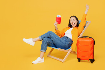Young winner woman in summer clothes sit in deckchair hold passport ticket isolated on plain yellow background. Tourist travel abroad in free spare time rest getaway. Air flight trip journey concept