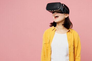 Young amazed surprised excited woman of Asian ethnicity wear yellow shirt white t-shirt watch in vr headset pc gadget isolated on plain pastel light pink background studio portrait. Lifestyle concept.
