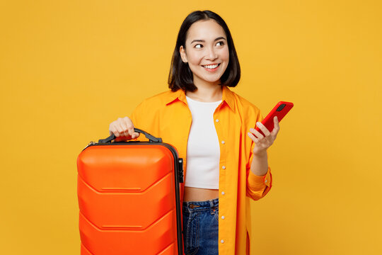 Young woman in summer casual clothes hold mobile cell phone bag look aside isolated on plain yellow background. Tourist travel abroad in free spare time rest getaway. Air flight trip journey concept
