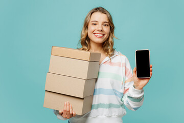 Fototapeta na wymiar Young blonde woman wears striped hoody use mobile cell phone with blank screen workspace area hold stack cardboard blank boxes isolated on plain pastel light blue cyan background. Lifestyle concept.