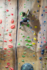 Young girl climbing up indoor rock climbing