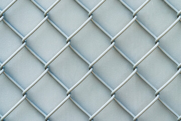 Closeup photograph of an old painted white and silver colored chainlink fence with crackled textured wind screen or tarp backdrop making a great background image.